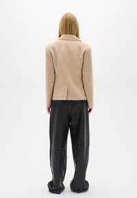 Béžový blazer z vlněné směsi s klopovým límcem, jedním rozventilovaným zadním dílem a dlouhými rukávy, v kombinaci s černými koženými kalhotami s vysokým pasem.