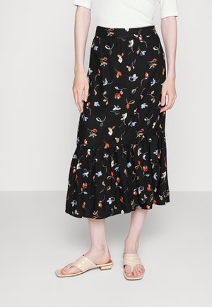 Saia preta floral com padrões coloridos, bainha com babados e cintura ajustada; combinada com sandálias de dedo em bege.