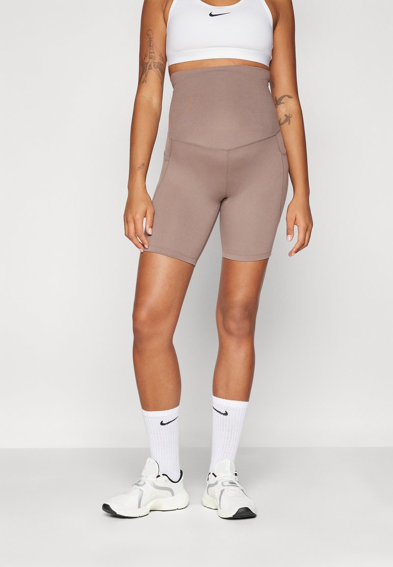Høyt liv, brune treningsshorts med en jevn tekstur og sidelommer, kombinert med en hvit sports-bh og hvite sokker med svarte detaljer.
