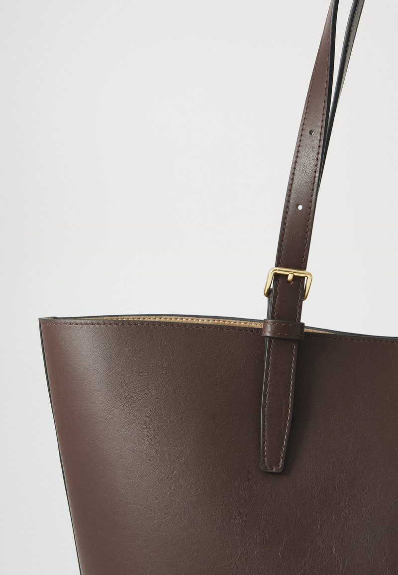 Braune Leder-Tote mit glatter Oberfläche, ausgestattet mit einem einzelnen Schulterriemen und goldenen Hardware-Details. Offenes Oberteil mit genähten Kanten.