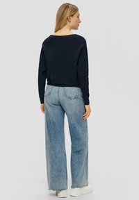 Marineblauer gerippter Strickpullover kombiniert mit hellblauen weitgeschnittenen Jeans und klobigen weißen Sneakern, von hinten betrachtet.