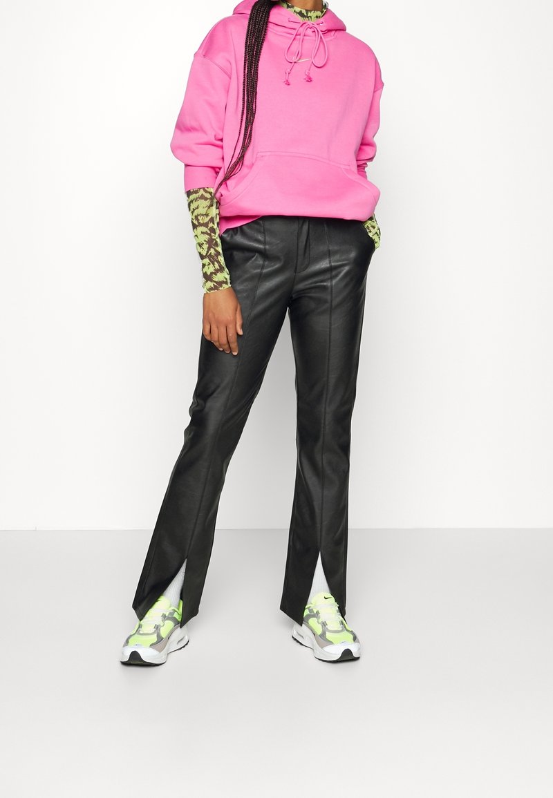 Pink hooded sweatshirt, black leather pants with side slits, and multicolored sneakers. The look features a patterned long-sleeve top underneath.