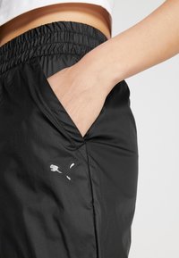 Svarta träningsshorts med elastisk midja och sidoficka, med en liten vit logotyp nära fickan. Slätt, lättviktigt tyg.