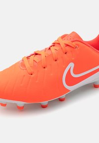 Lys oransje Nike fotballsko med en glatt syntetisk overdel, teksturert detaljering og en hvit swoosh-logo. Har hvite og røde knotter.