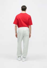 Rotes Baumwoll-T-Shirt mit kurzen Ärmeln, kombiniert mit hellgrauen Jogginghosen mit elastischem Bund und Gesäßtasche. Weiße Sneakers.