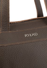 Brązowa torba na ramię z teksturowanym wykończeniem, z jaśniejszym brązowym przeszyciem i srebrnym logo RYLKO z przodu.