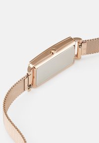Rechteckige Uhr mit einem glatten, goldfarbenen Metallgehäuse und einem feinen Mesh-Armband. Die Rückseite ist blank und verfügt über eine einfache Druckknopfkrone.
