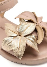 Infradito marroni chiari con una fascia larga e un grande dettaglio floreale metallico dorato sul davanti, caratterizzato da petali in pelle testurizzata e un design morbido.