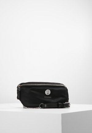 Schwarze rechteckige Bauchtasche mit silbernem Reißverschluss, Löwenemblem, "VERSUS"-Schriftzug und verstellbarem Gurt mit Kettendetail auf weißer Oberfläche.