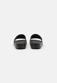 Svarta sandaler med öppen bakdel, tillverkade av texturerat syntetmaterial; har en enkel design med breda remmar och en platt gummisula.