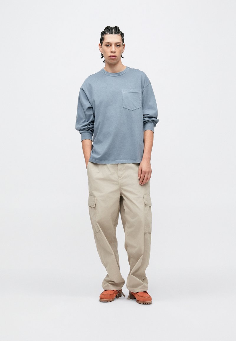 Blå långärmad skjorta med bröstficka, kombinerad med beige cargobyxor och orange skor. Outfiten har en avslappnad passform och mjuka texturer.