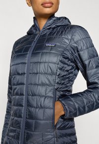 Λουστρινένιο μπουφάν σε ναυτικό μπλε χρώμα με φερμουά ρ μπροστά, καπιτονέ υφή και κουκούλα. Διαθέτει πλαϊνές τσέπες και μικρό λογότυπο Patagonia στο στήθος.