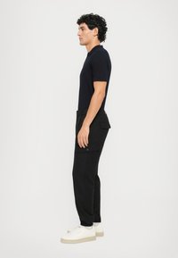Marineblå kortærmet polo skjorte parret med sorte cargo bukser med sidelommer og elastiske manchetter, suppleret med hvide sneakers.