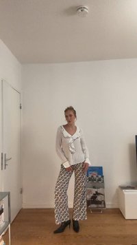 Balta palaidinė su raukiniais priekyje ir juoda apdaila, derinama su plačiomis mėlynomis ir baltomis raštuotomis kelnėmis. Juodi smailiakulniai bateliai baigia aprangą.