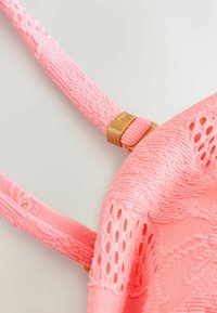 Bandoulière en tissu texturé rose avec boucle réglable dorée attachée à un matériau en dentelle à motifs.
