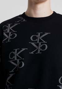 Felpa nera con un motivo a logo argentato ripetuto. Realizzata in materiale morbido, con collo rotondo e polsini a coste.