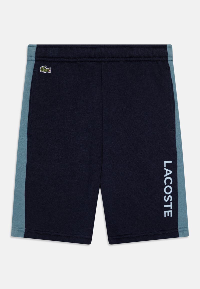 Tumši jūras zila šorti ar gaiši teal krāsas sānu paneļiem, elastīga jostasvietā, sānu kabatām un ar baltu tekstu "LACOSTE" labajā kājā.