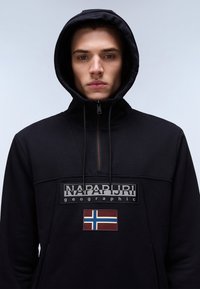Sudadera con capucha negra con cuello con cremallera, un parche con logotipo y un detalle de la bandera noruega en la parte delantera, fabricada en un tejido suave.