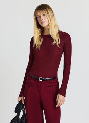 Top bordeaux a maniche lunghe con texture liscia; abbinato a pantaloni bordeaux con tasche frontali e cintura nera; tiene una borsa nera.