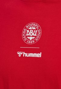 Roter Stoff mit weißem, rundem Dansk Boldspil-Union 1889 Logo über einer horizontalen Linie und dem Hummel Markenlogo darunter.
