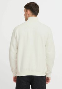 Sweatshirt beige clair avec un col haut, des poignets et une taille côtelés. Fabriqué en tissu doux en mélange de coton, avec un design uni.