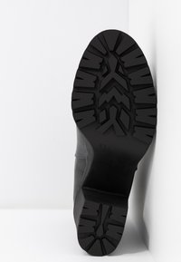 Černá bota s texturovanou gumovou podrážkou, která má cik-cak vzor a hladký kožený svršek. Velikost je označena jako 37.