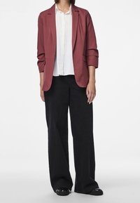 Blazer rouge sur une chemise blanche, associé à un pantalon noir ample. Présente une coupe ajustée, une texture lisse et des détails de couture subtils.