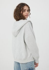 Felpa grigia chiara con cappuccio realizzata in morbido cotone misto. Caratterizzata da una vestibilità rilassata, maniche ampie e una tasca a marsupio.