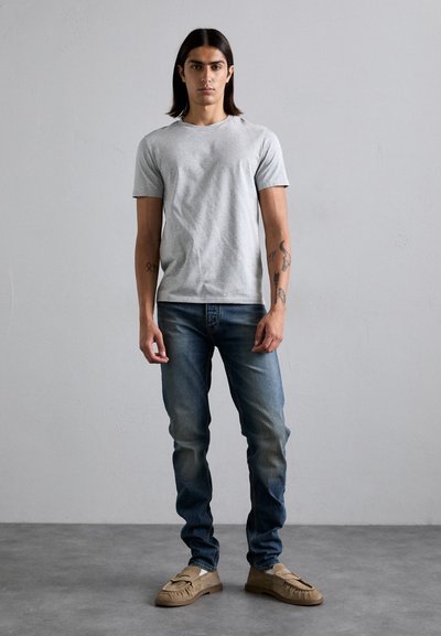 T-shirt cinza de algodão, design ajustado, combinado com jeans azul de denim. Calçado com mocassins de suede bege. Roupa minimalista e casual.