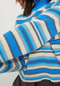 Strickpullover mit breiten horizontalen Streifen in Blau, Weiß und Grau. Hoher Kragen und lockere Passform mit einem strukturierten Stoffdesign.