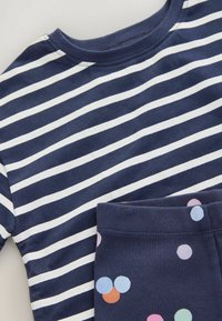 Gestreiftes navyblaues Baumwollhemd mit weißen Streifen, kombiniert mit navyblauen Hosen, die bunte Punkte in Pastellfarben aufweisen. Weiche Textur und gerippte Details.