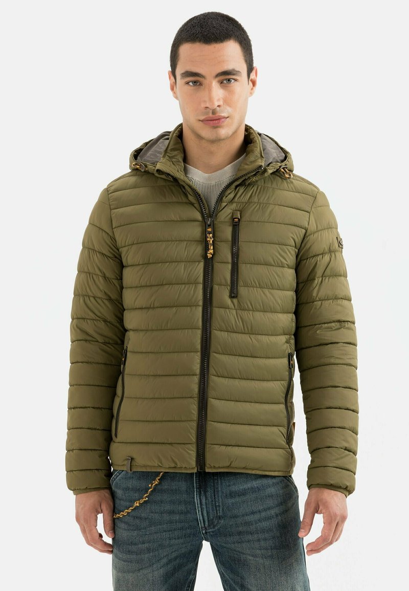Olivgrüne Pufferjacke mit Kapuze, vertikalen Nähten, Frontreißverschluss und zwei Seitentaschen. Mit grauem Innenfutter und kontrastierender Hardware.