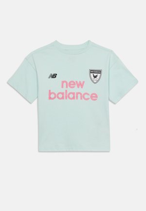 Lys blå T-skjorte med korte ermer, rosa "new balance"-tekst, svart "NB"-logo på venstre side, og svart-hvitt "new balance" skjoldemblem på høyre bryst.