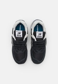 Baskets noires avec un dessus en maille et en daim, dotées d'une sangle velcro, d'accents blancs et d'un col rembourré. Étiquette New Balance sur la languette.