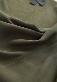 Olive green fabric with a smooth texture, featuring soft folds and subtle diagonal line patterns. The edges are neatly finished.