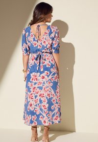 Blaues Midi-Kleid mit pinken Mustern, kurzen Puffärmeln, offener Rückseite und Bindeband in der Taille. Leichter Stoff mit fließender Textur.