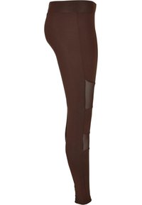 Leggings marron avec un design ajusté, dotés de panneaux en mesh transparent sur les côtés. Fabriqués en tissu extensible, avec une texture douce.