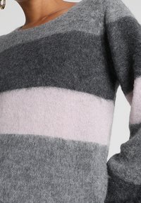 Strickpullover mit horizontalen Streifen in Dunkelgrau, Hellgrau und zartem Rosa. Weiche, flauschige Textur mit lockerem Schnitt.