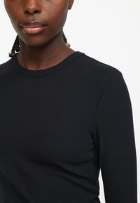 Sort ribbet langærmet skjorte med rund hals, med et tætsiddende design og blød tekstur. Stoffet har let stræk og en glat finish.