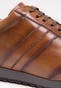 Braune Lederschuhe mit glatter Textur, drei vertikal genähten Linien, dunkelbraunen Schnürsenkeln und einer schwarzen Gummisohle.