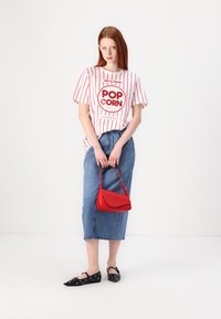 Valkoinen t-paita punaisilla raidoilla ja "POP CORN" -grafiikalla; sininen farkkupitkä hame; punainen käsilaukku; mustat ballerinat, joissa on pilkkuja.