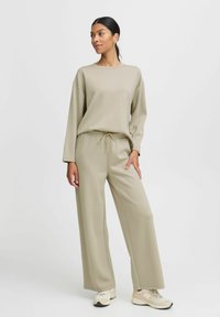 Conjunto de sudadera beige y pantalones de pierna ancha, hecho de material suave, con cuello redondo y cintura con cordón, combinado con zapatillas en tonos neutros.