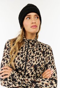 Langarm-Zip-Up-Top mit schwarz-braun-beigem Animalprint; weicher Stoff; hoher Kragen; Modell trägt eine schwarze Strickmütze.