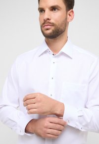 Wit overhemd met knopen, uitgevoerd in een getextureerde stof, met een spitse kraag en een borstzak, voorzien van metalen knopen op de manchetten.