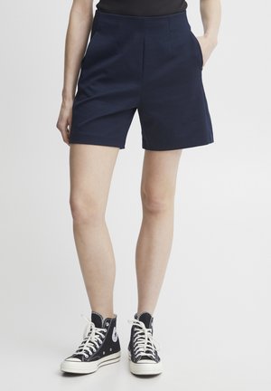 Marineblauwe hooggetailleerde shorts van katoenmix, met twee zijzakken, een gladde textuur en een op maat gemaakte pasvorm. Gecombineerd met zwarte sneakers.