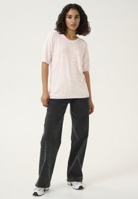 T-shirt rose clair avec un motif subtil, à manches courtes, associé à un jean noir clair et des baskets blanches.