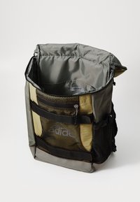 Sac à dos en tissu gris et doré avec une poche avant en maille, fermeture éclair et bretelles réglables. Intérieur doublé d'un matériau gris lisse.