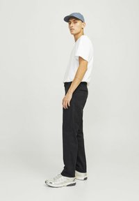 Weißes T-Shirt mit kurzen Ärmeln, schwarze Hose, graue Mütze und silberne Sneaker. Lässiges Outfit mit einfachem Design, figurbetontem Schnitt und klaren Linien.