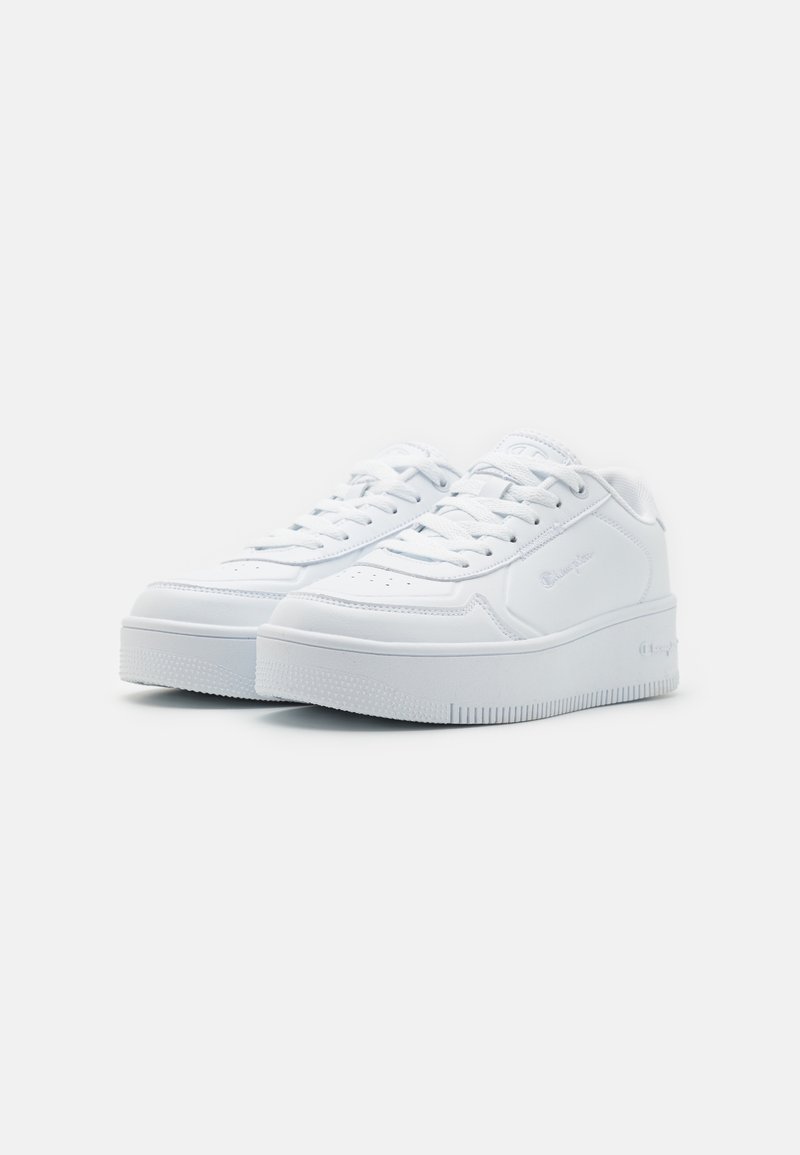 Sneakers atletici bianchi con tomaia sintetica liscia, lacci piatti e suola in gomma testurizzata. Presentano un logo discreto sul lato.