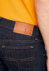 Mörka jeans i denim med orangea sömmar, som har en brun läderlapp på bakre midjan, synliga fickor och en figurnära silhuett.